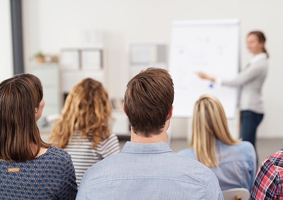Eine Dozentin steht vor einer Gruppe an einem Flipchart