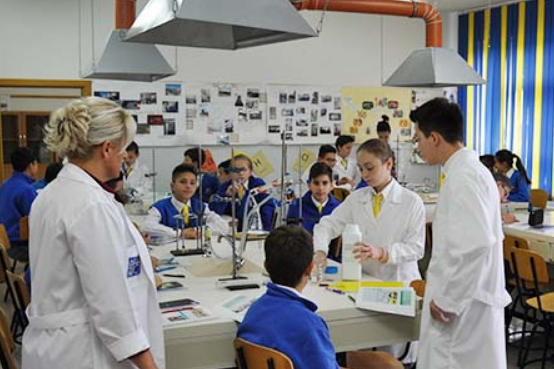 Lehrerin schaut Schülerinnen und Schülern zu, wie sie einen Versuch im Chemieunterricht durchführen